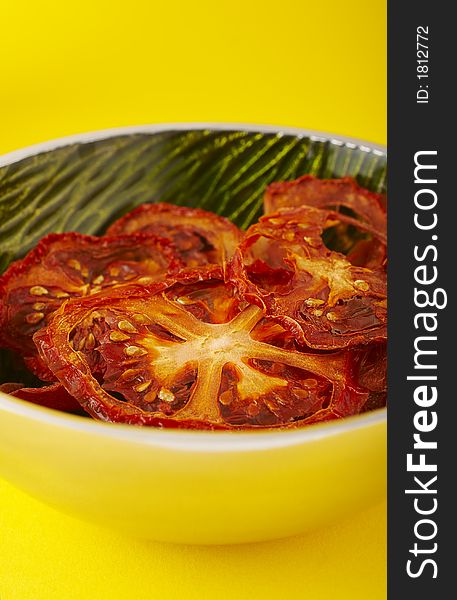 Dried sliced tomatoes in green bowl on the yellow background. Dried sliced tomatoes in green bowl on the yellow background.