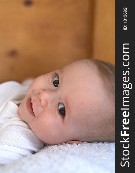 Image of baby boy wearing a white onesie lying on a bed. Image of baby boy wearing a white onesie lying on a bed