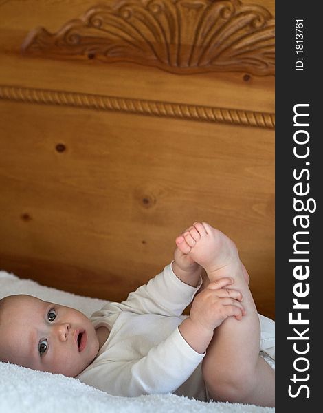 Image of baby boy wearing a white onesie lying on a bed playing with his feet. Image of baby boy wearing a white onesie lying on a bed playing with his feet