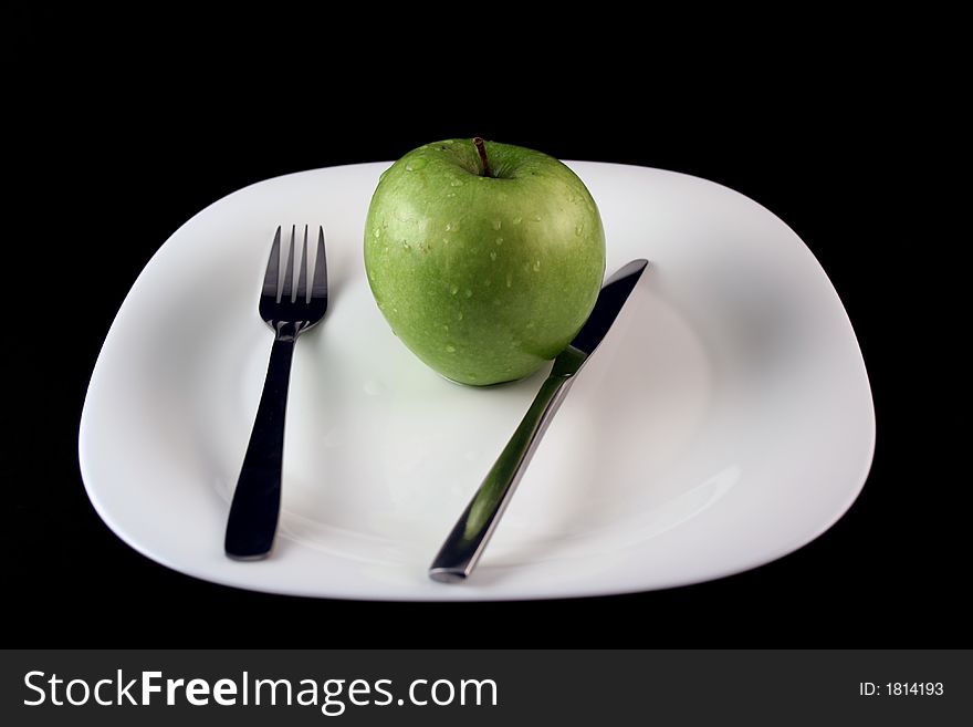 Green apple on a plate with fork and knife