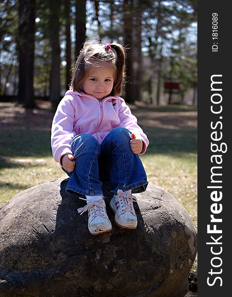 Four year old girl sitting on a rock in a park. Four year old girl sitting on a rock in a park.
