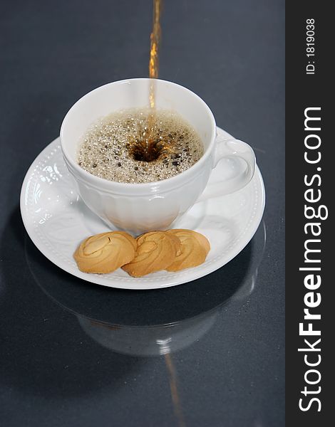 Pouring coffee into coffee cup and cookies isolated on black