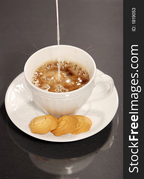 Pouring milk into coffee and cookies isolated on black