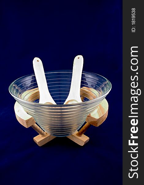 A glass salad platter with wooden cutlery and wooden support isolated on dark blue background.