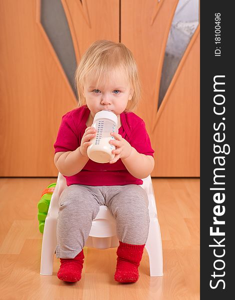 Adorable baby sit on baby chair toilet and drink milk from bottle
