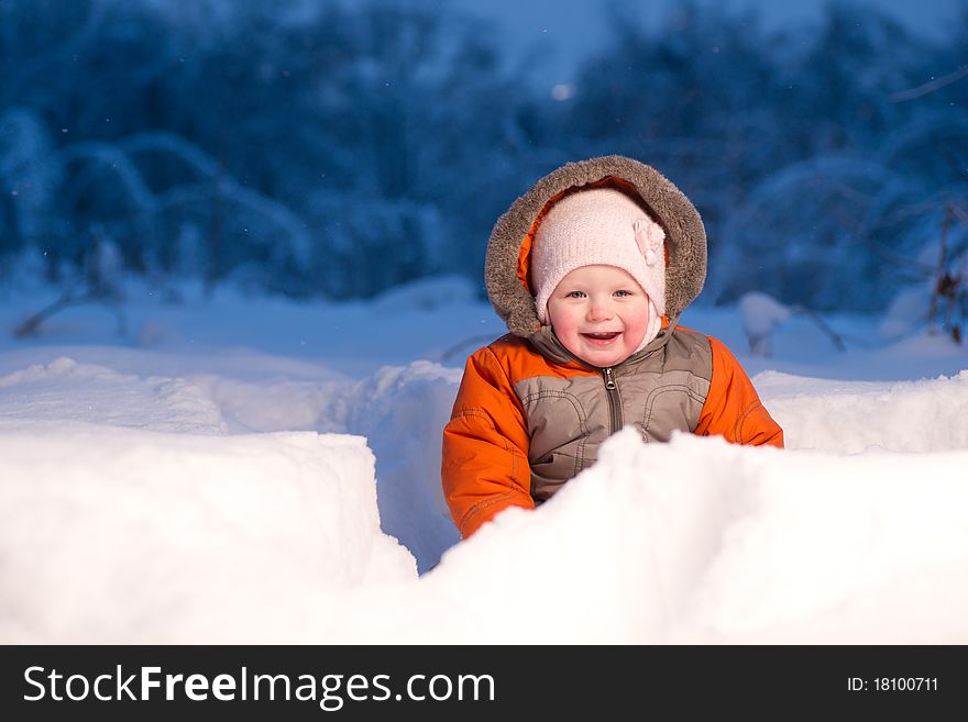 Adorable baby sit and digging hideout hole in snow in field in the evening park