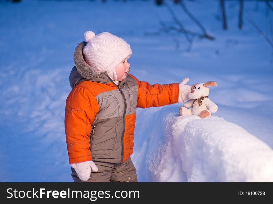 Cute baby touch toy dog sitting on snow in winter park in evening. Cute baby touch toy dog sitting on snow in winter park in evening