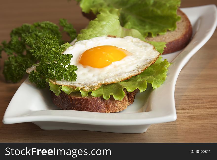 Sandwich with a fried egg on a white plate on a wooden surface. Sandwich with a fried egg on a white plate on a wooden surface