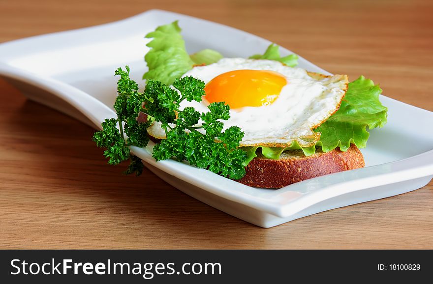 Sandwich with a fried egg on a white plate on a wooden surface