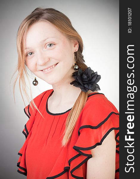 Beautiful blond woman wears red dress, smells black flower, with grey background