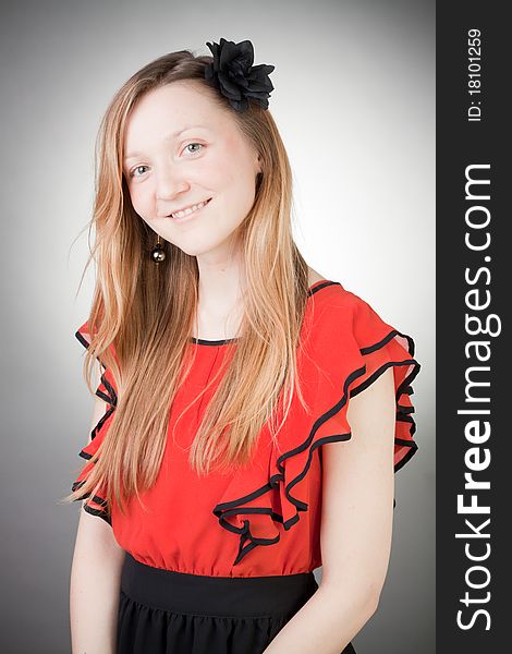 Beautiful blond woman wears red dress, smells black flower, with grey background