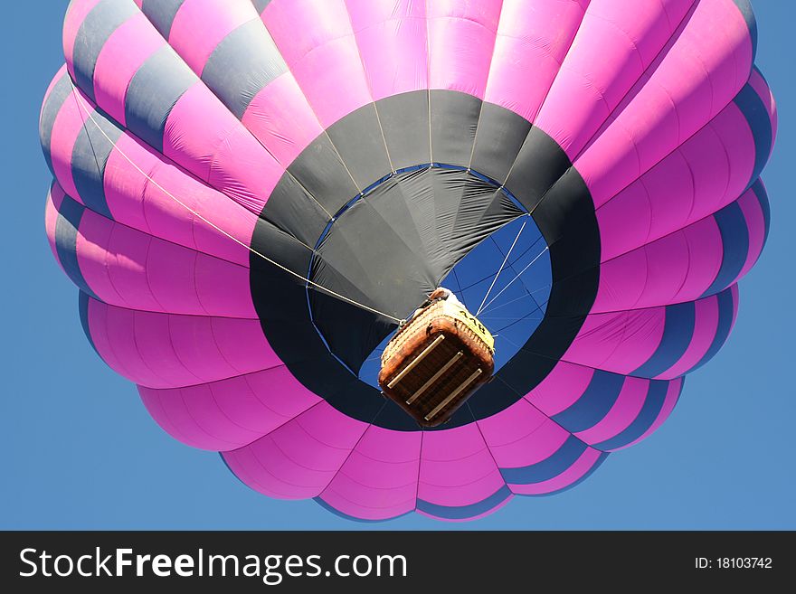 Low angle view of pink hot air balloon in flight with blue sky background.