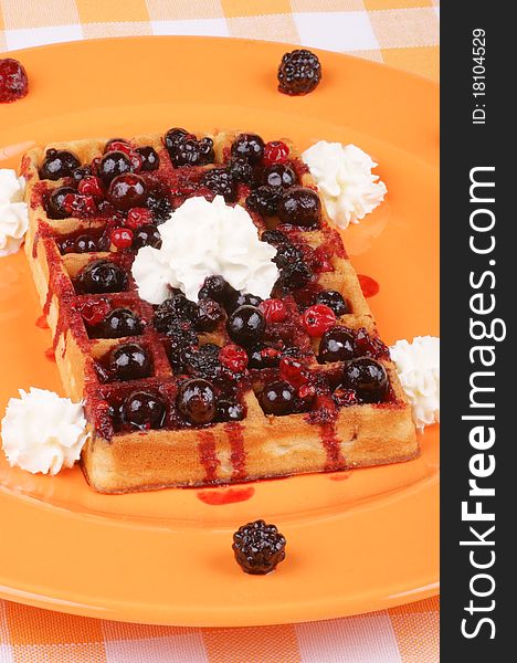 Waffle with soft fruits and whipped cream on an orange plate