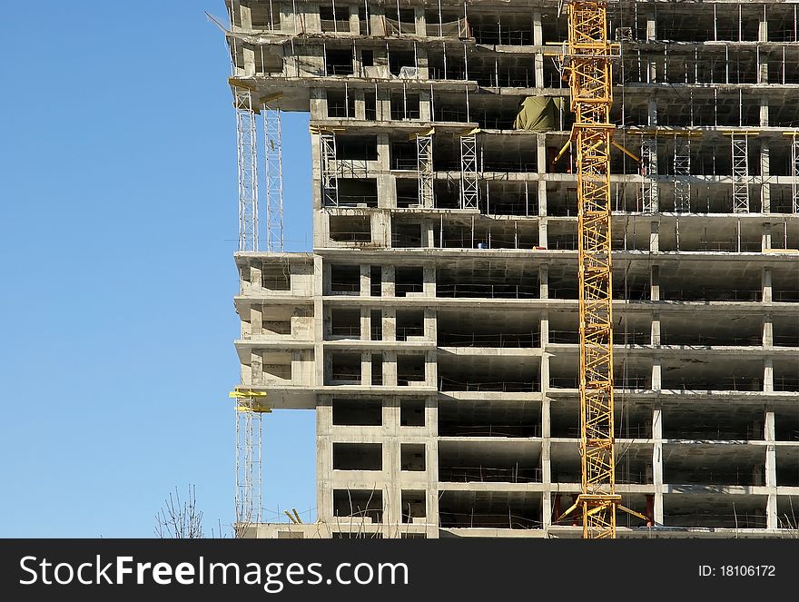 Elevating construction crane and building under construction on the blue clear sky