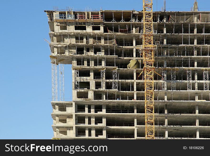 Elevating construction crane and building under construction on the blue clear sky