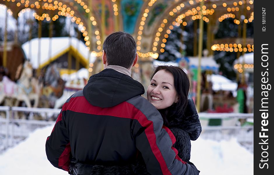 Happy couple looking at carousel in winter time