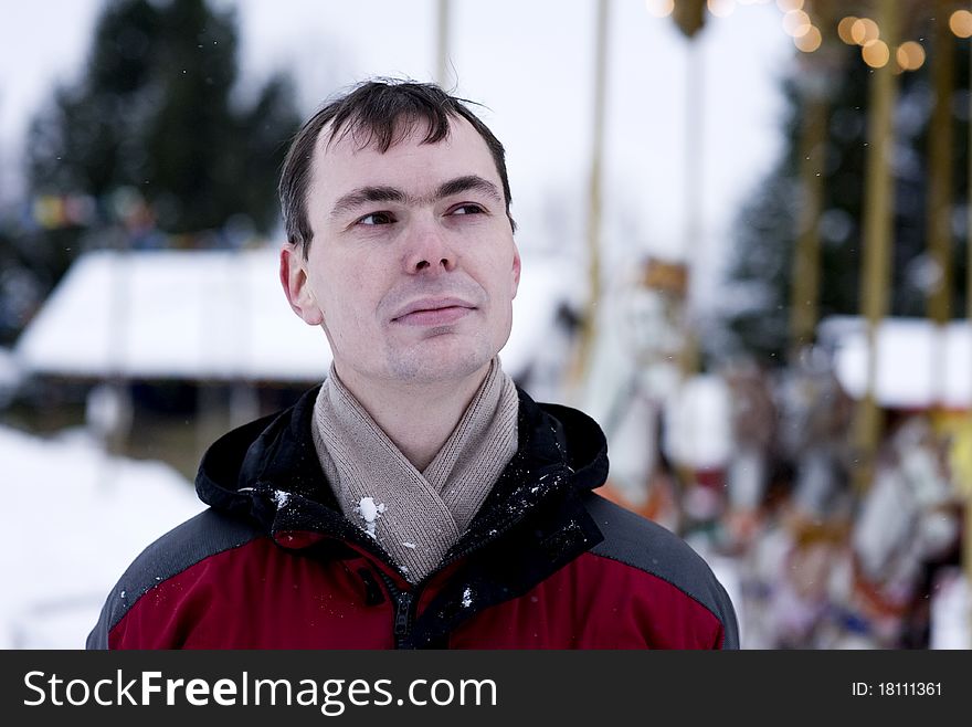 Portrait of adult man in winter time with carousel on background