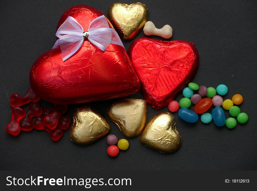 Two chocolate hearts covered with red shiny paper, one with a white silk bow, plus four small gold chocolate hearts and some candy. A gift for Valentine's Day. Two chocolate hearts covered with red shiny paper, one with a white silk bow, plus four small gold chocolate hearts and some candy. A gift for Valentine's Day.