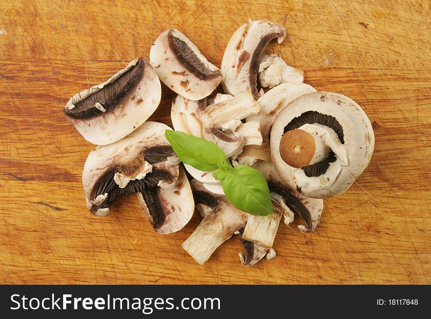Sliced and whole mushrooms with basil on a worn food preparation board. Sliced and whole mushrooms with basil on a worn food preparation board