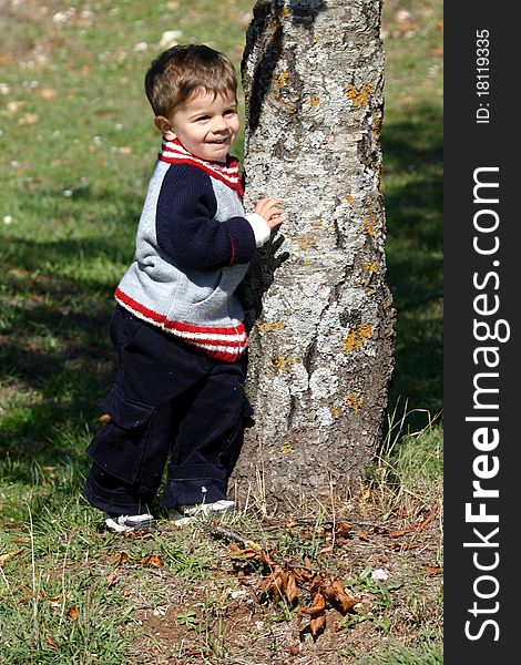 A little boy standing by a tree in the park. A little boy standing by a tree in the park.
