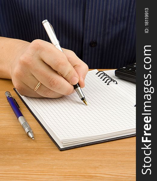 Male hand writing by pen on checked notebook. Male hand writing by pen on checked notebook