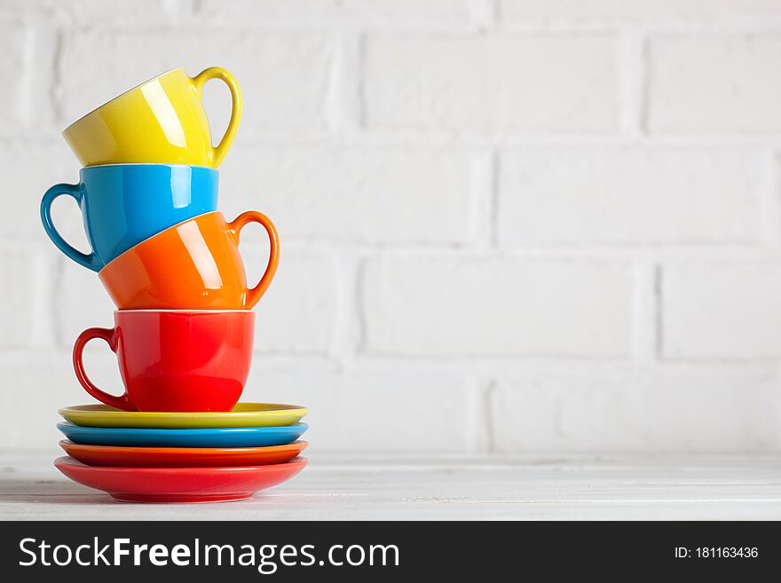 Colorful cups on the white background of a brick wall. Background with copy space. Horizontal. Selective focus.