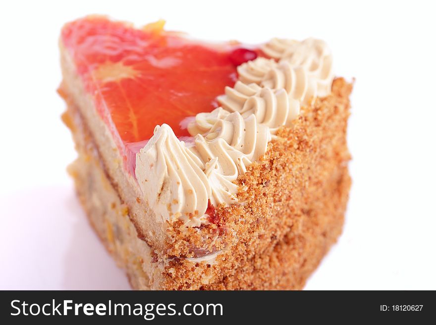 Piece of delicious cake with whipped cream garnished with fruits in jelly isolated on white background. Piece of delicious cake with whipped cream garnished with fruits in jelly isolated on white background