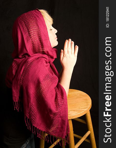 Woman wearing red scarf praying, black background. Woman wearing red scarf praying, black background