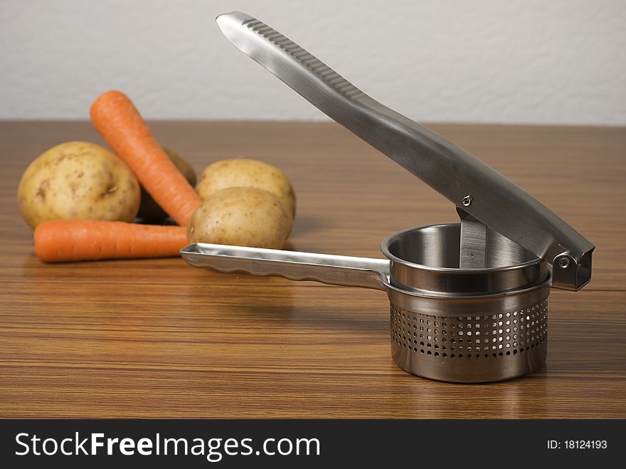 A horizontal image of a food ricer masher and vegetables on a wooden table. A horizontal image of a food ricer masher and vegetables on a wooden table