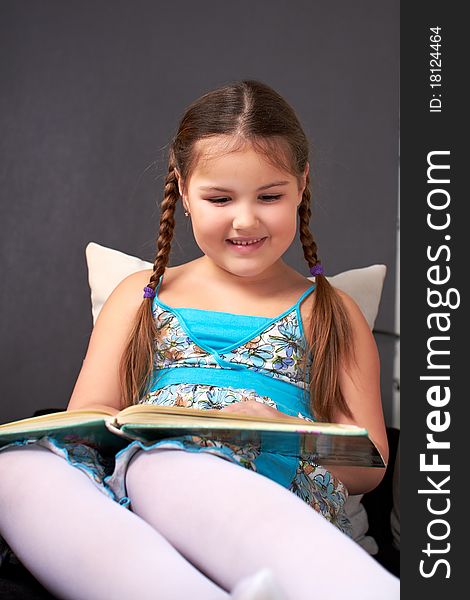 The little girl dreamily sits on the couch with book.