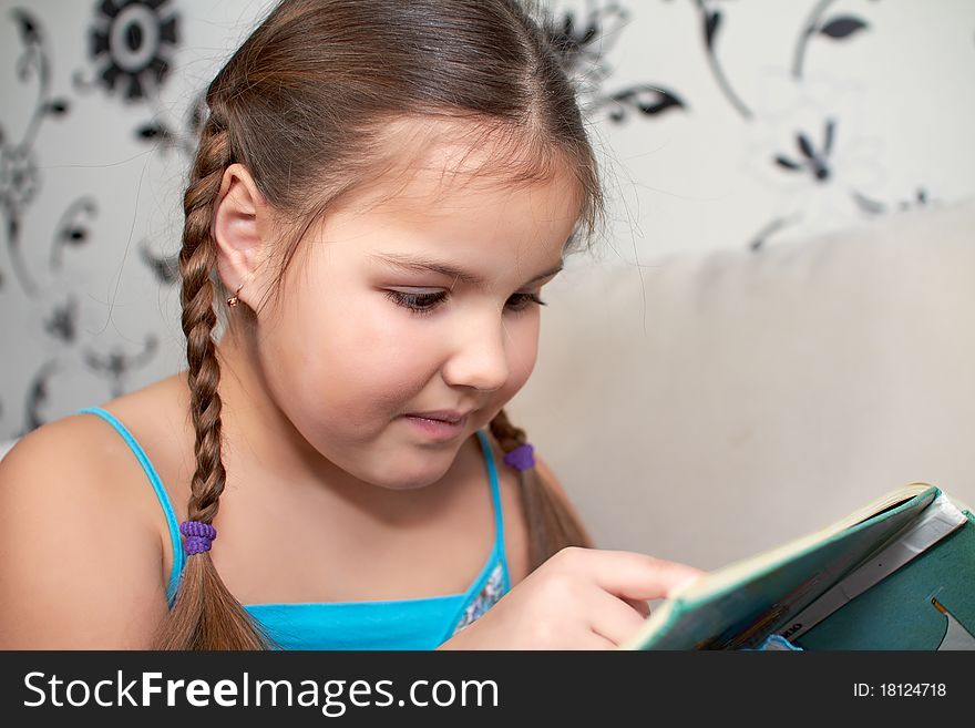 The little girl dreamily sits on the couch with book. (picture with a small depth of field)