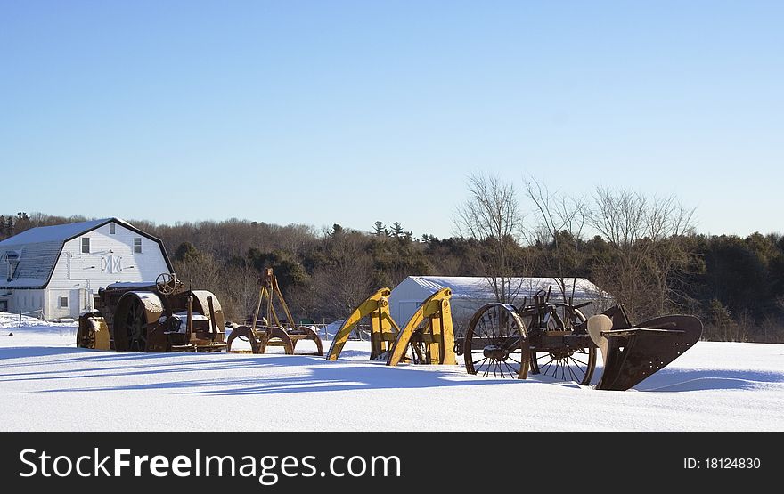 Snow covered antique farm equipment in morning sun with barns. Snow covered antique farm equipment in morning sun with barns