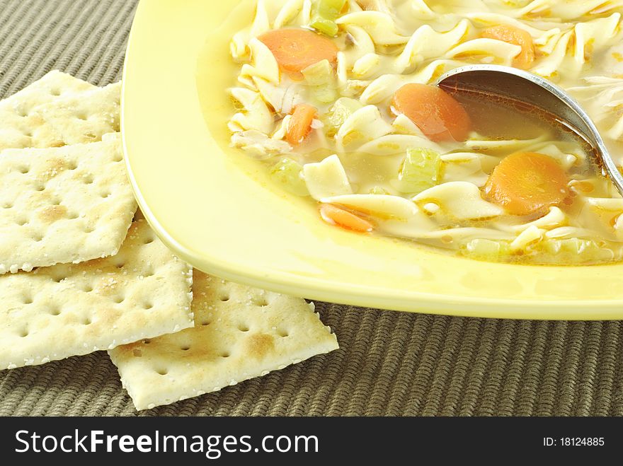 A bowl of hot homemade chicken noodle soup with crackers, horizontal with copy space