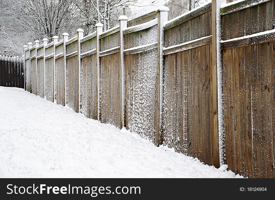 A large eight foot wooden fence in a back yard covered with snow, horizontal with copy space. A large eight foot wooden fence in a back yard covered with snow, horizontal with copy space