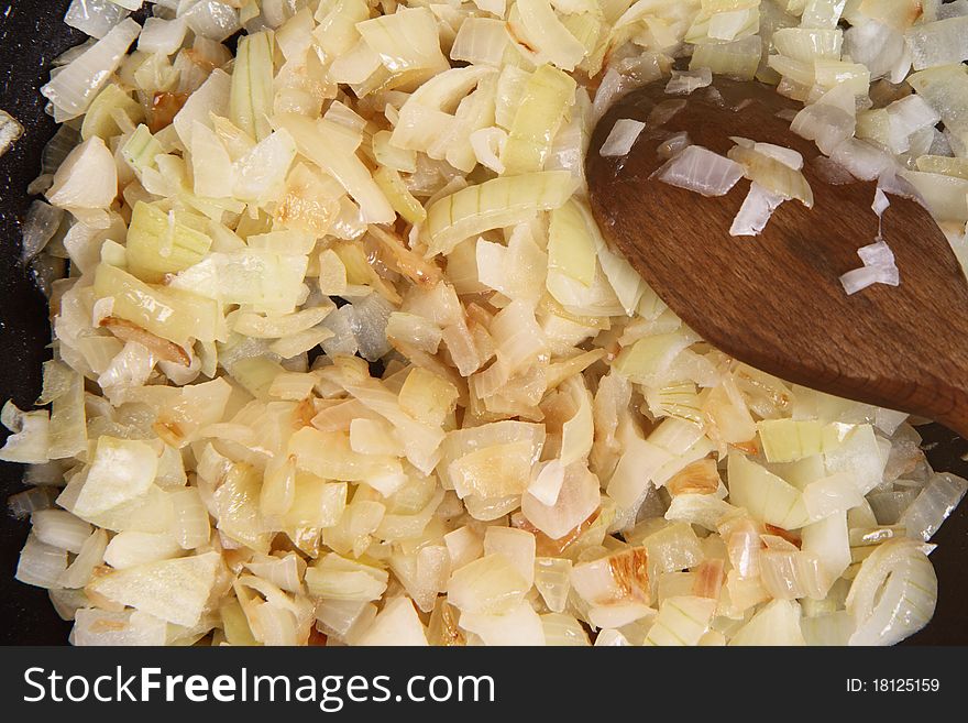 Onion being fried on a pan with a ladle