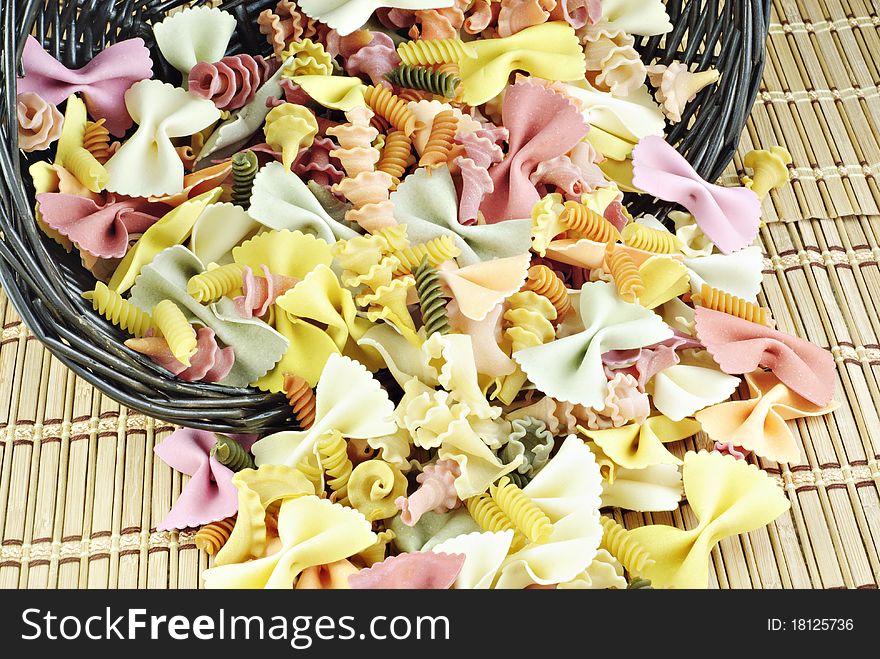 Colorful vegetable pasta spilling out of a basket, textured background