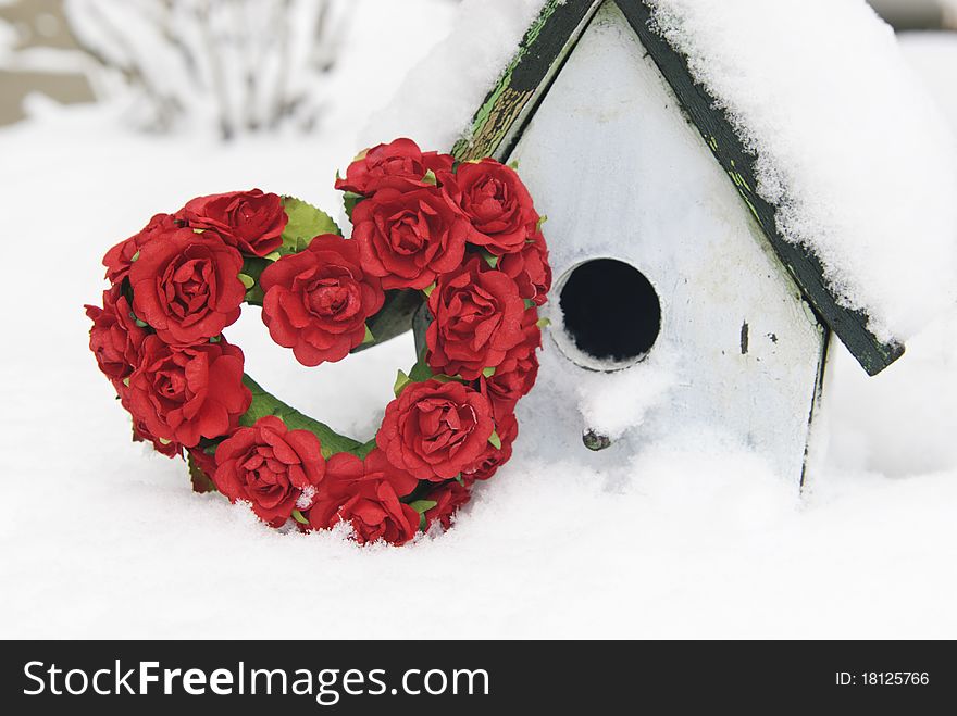 A red rose Valentine heart with a birdhouse in the snow, shallow depth of field with copy space. A red rose Valentine heart with a birdhouse in the snow, shallow depth of field with copy space