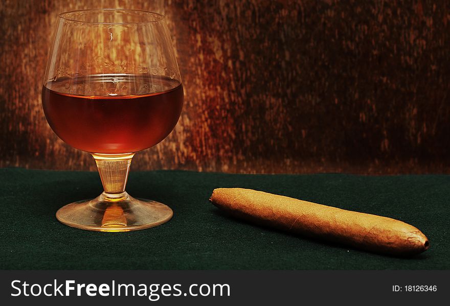 Cigar and a glass of alcohol on green fabric