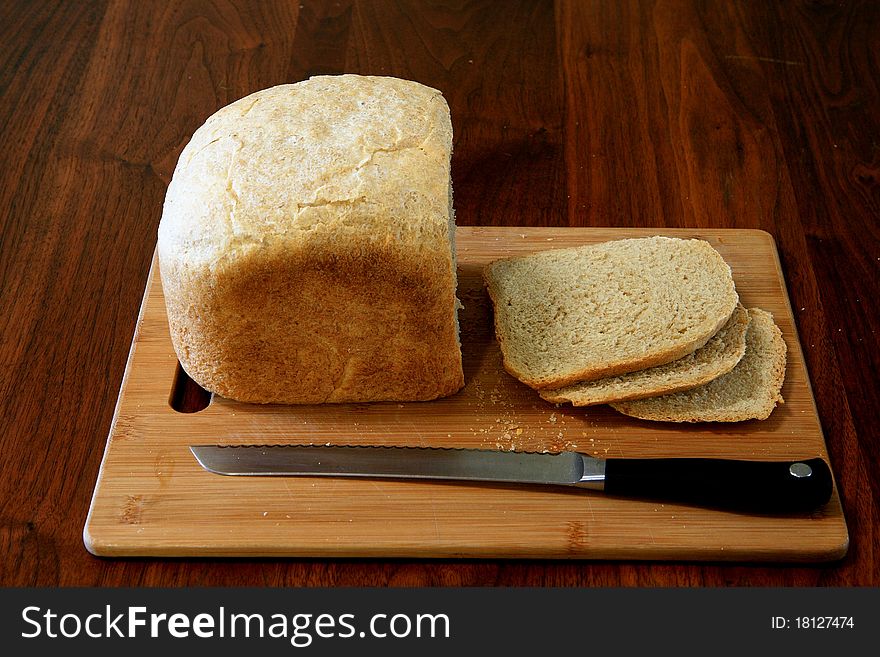 A loaf of homemade bread on a cutting board with a knife and a few slices