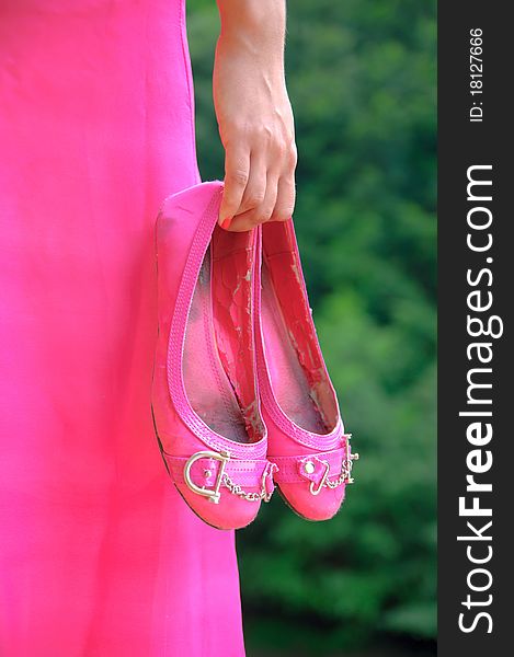 Hand of a young girl dressed in pink dress holding a pair of shoes on green background. Hand of a young girl dressed in pink dress holding a pair of shoes on green background.