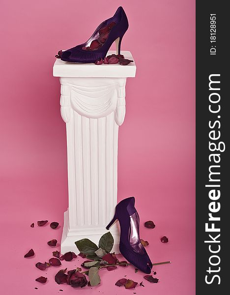 Purple high-heel shoes on pedestal with rose petals and a dying rose. Purple high-heel shoes on pedestal with rose petals and a dying rose