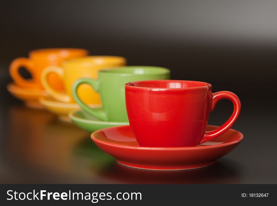 Four multi-colored ceramic cups are one after another on a black background. Four multi-colored ceramic cups are one after another on a black background