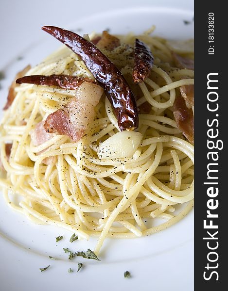 Fusion food of spicy pasta bacon on white plate.