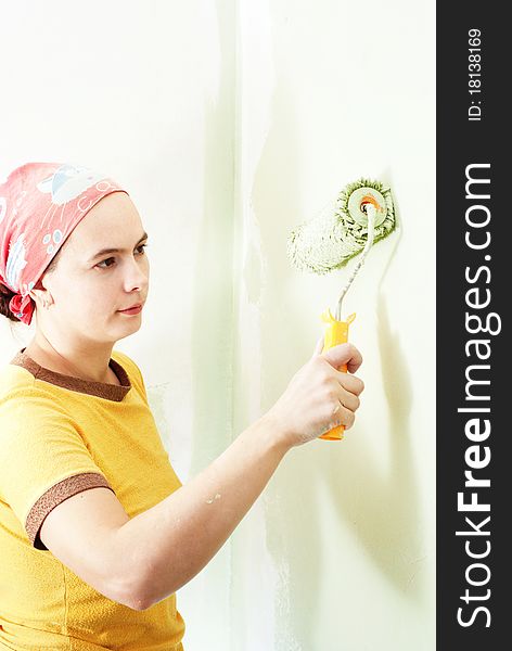 Young woman painting white wall with green paint. Young woman painting white wall with green paint