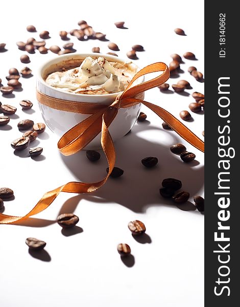 Cup of coffee with cream, coffee beans and golden ribbon