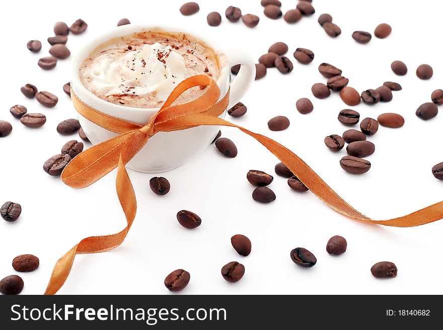 Cup of coffee with cream, coffee beans and golden ribbon