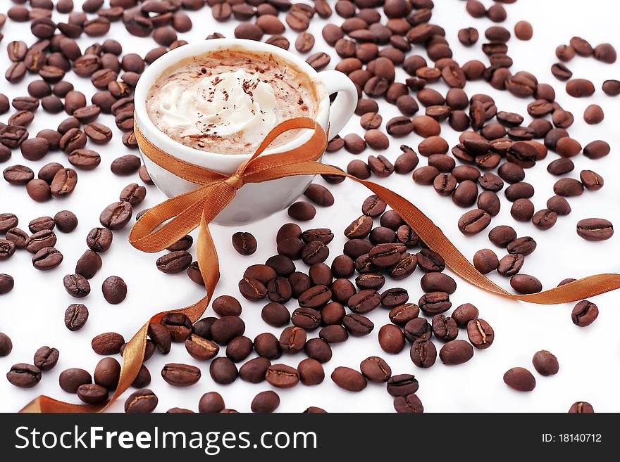 Cup of coffee with cream, coffee beans and golden ribbon