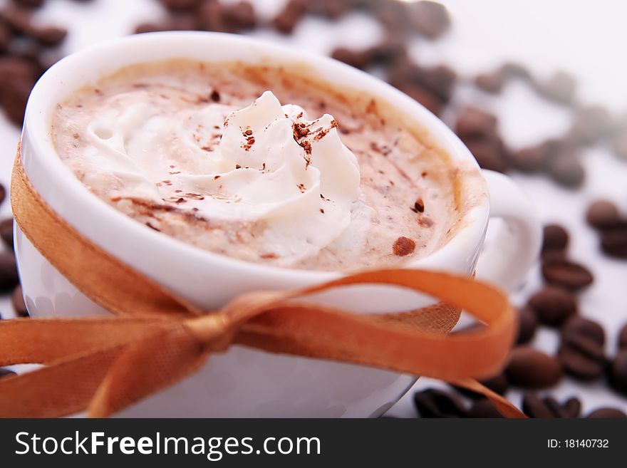 Cup of coffee with cream, coffee beans and golden ribbon close-up