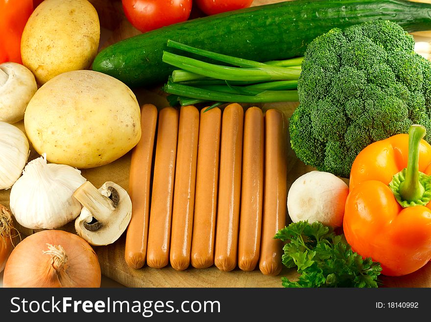 A bunch of fresh frankfurter sausages on the wooden board with raw fresh healthy vegetables