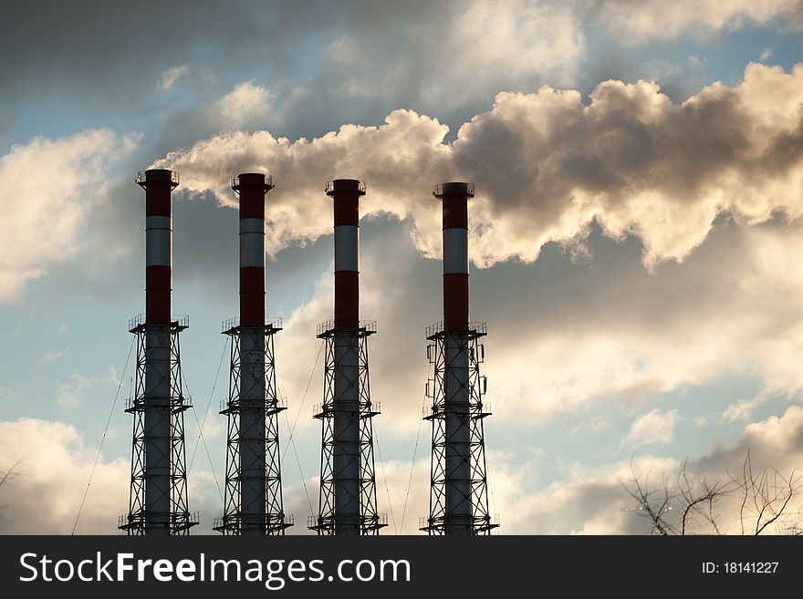 Pipes with smoke on blue sky background with clouds